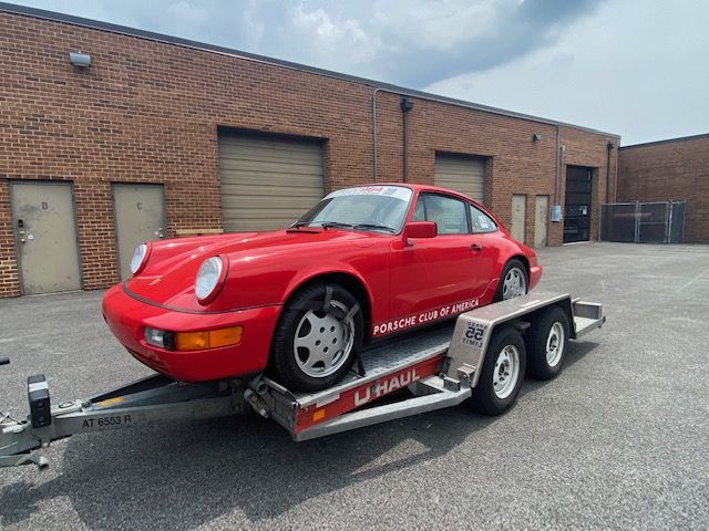 Roter Porsche 911 auf einem Autoanhänger vor einem Backsteingebäude.