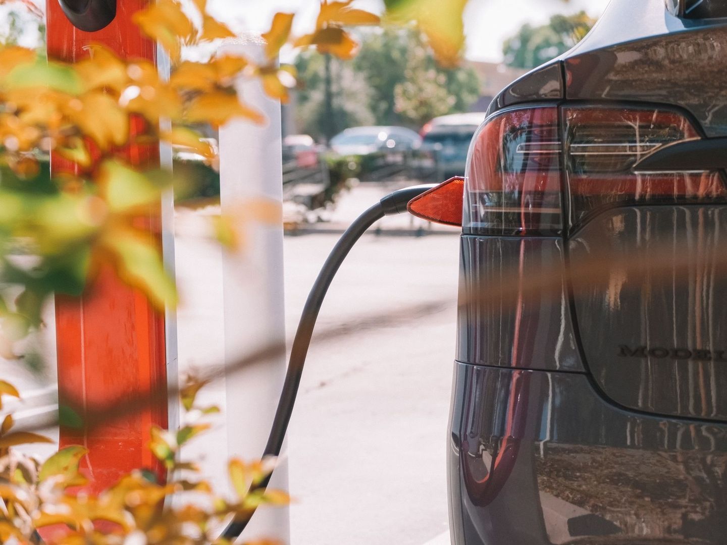 Elektroauto lädt an einer Ladestation unter herbstlichen Bäumen