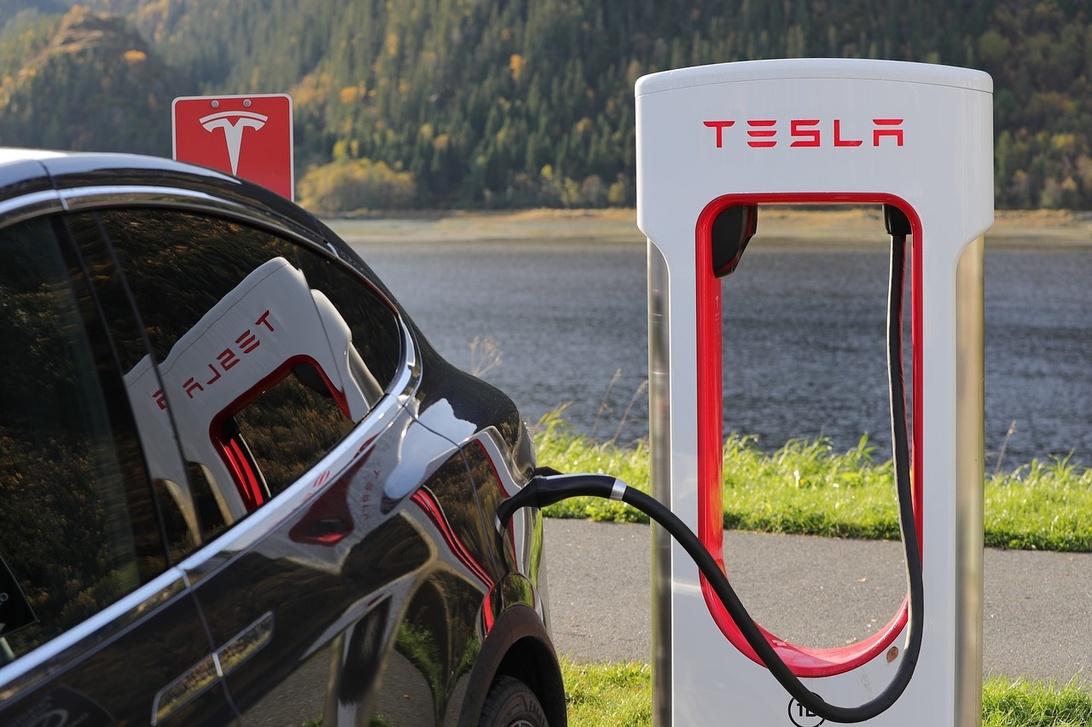 Elektromobilität und nachhaltige Infrastruktur: Ein Tesla lädt vor malerischer Kulisse und unterstreicht die Bedeutung von Leichtbau für die Reichweite von E-Autos.